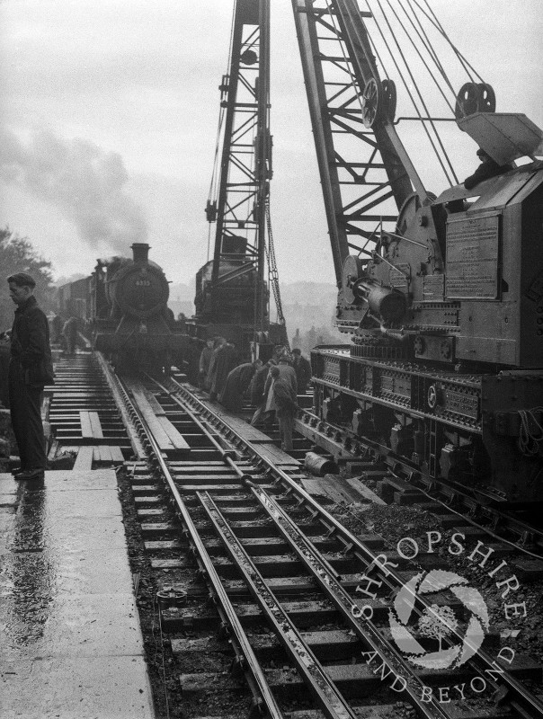 A steam train passes two cranes on the railway bridge, Shifnal, Shropshire, 1953.