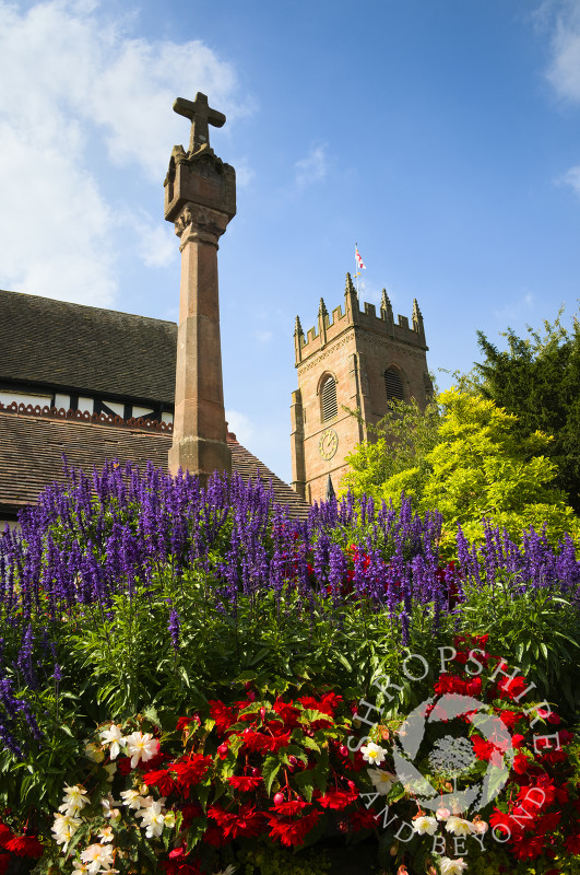 Flowers surround the 14th century cross at the entrance to All Saints Church, Claverley, Shropshire, England.