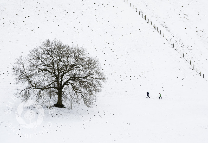 Walkers in snow beneath Gaer Stone, near Church Stretton, Shropshire, England.