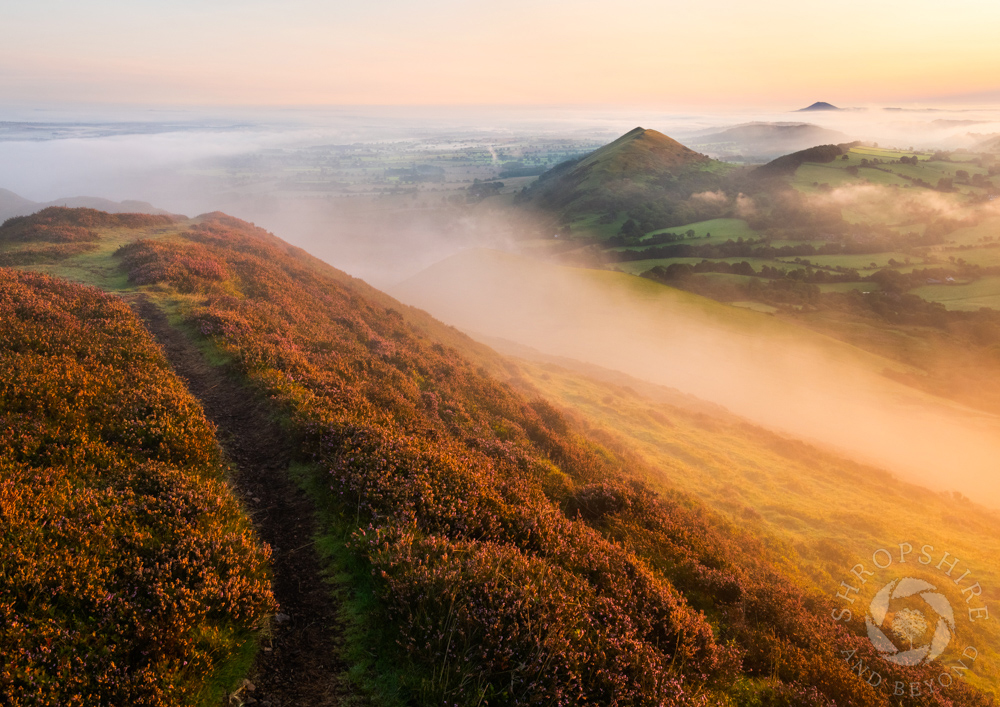 A path along the ramparts on Caer Caradoc, with the Lawley and the Wrekin amid the mist.