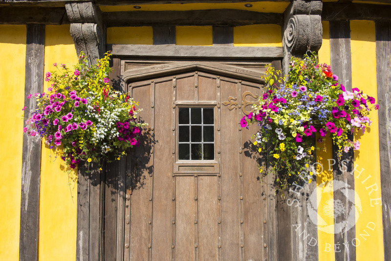 Hanging baskets adorn the front door of a half-timbered house in Broad Street, Ludlow, Shropshire, England.