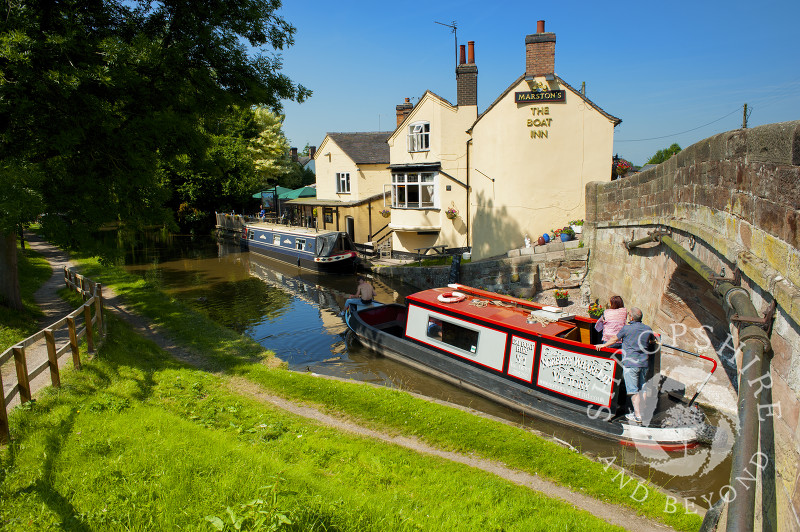 A narrowboat passes the Boat Inn at Gnosall on the Shropshire Union Canal, Staffordshire, England.