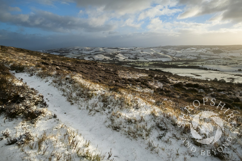 A snow-covered path on the Stiperstones with the Long Mynd seen in the distance, Shropshire.
