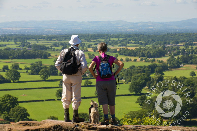 Two walkers and their dog look out over the north Shropshire landscape from Grinshill Hill, Shropshire, England.