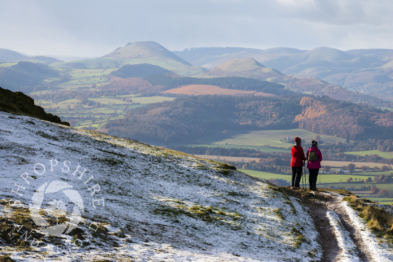 Two walkers look out over the Shropshire Hills from a snow-covered Wrekin, Shropshire.