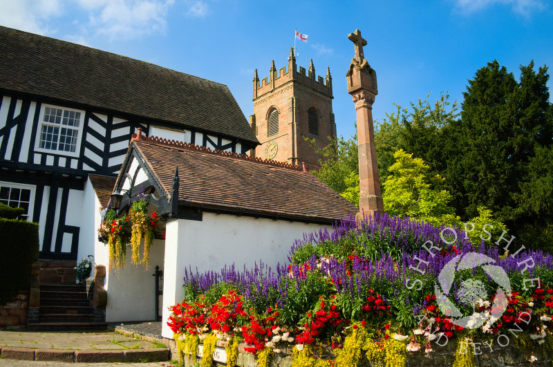 Flowers surround the 14th century cross at the entrance to All Saints Church, Claverley, Shropshire, England.