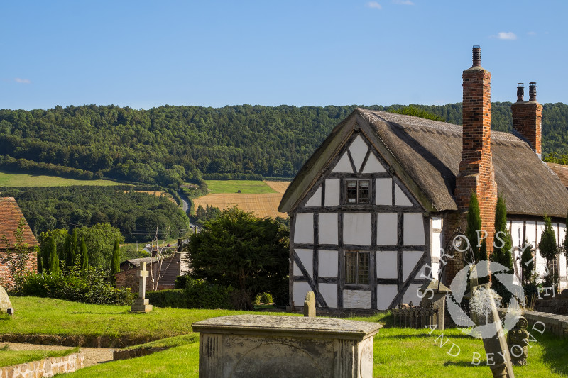 A black and white thatched cottage with Wenlock Edge in the distance, seen from St Mary's Church, Harley, Shropshire.