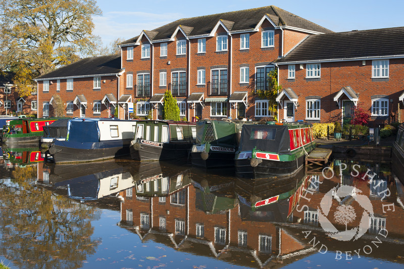 Canal boats and homes reflected in the Shropshire Union Canal at Market Drayton, Shropshire, England.