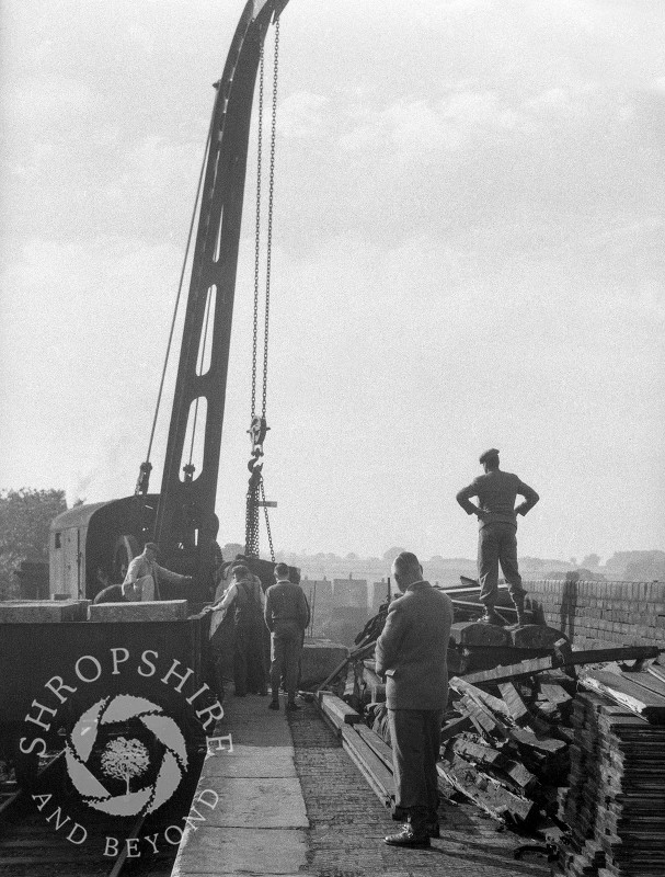 Workmen watch a crane in operation, Shifnal, Shropshire, 1953.