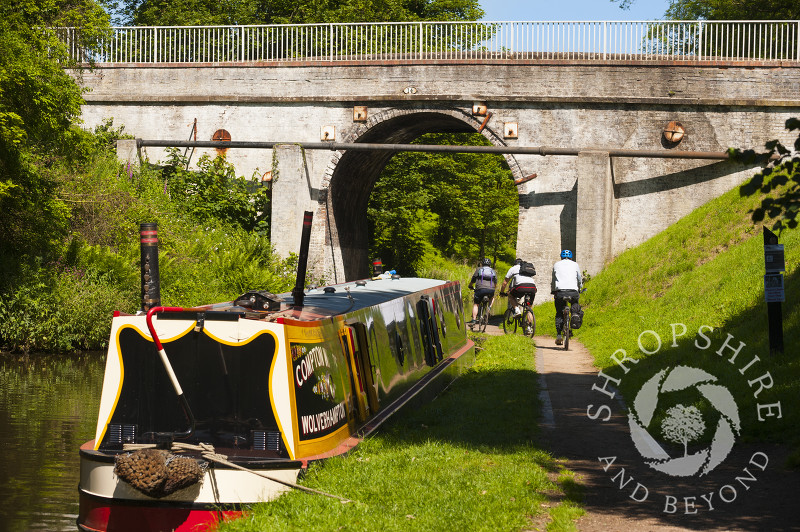 Cyclists ride past a moored canal boat on the Shropshire Union Canal at Brewood, Staffordshire, England.