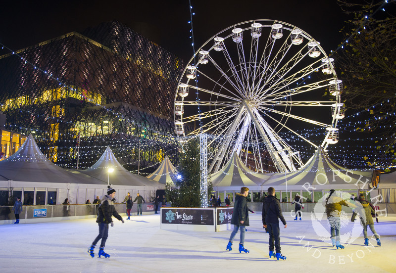 Skaters on the ice rink in Centenary Square in front of the Big Wheel and Library of Birmingham during the Frankfurt Christmas Market, Birmingham, West Midlands, England.