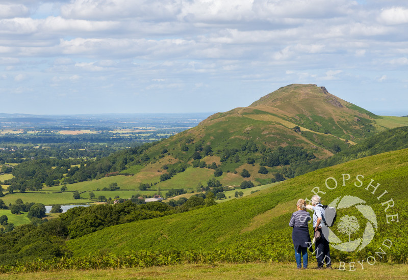 Two walkers on Ragleth Hill enjoy the views of the surrounding Shropshire countryside with Caer Caradoc, at Church Stretton.