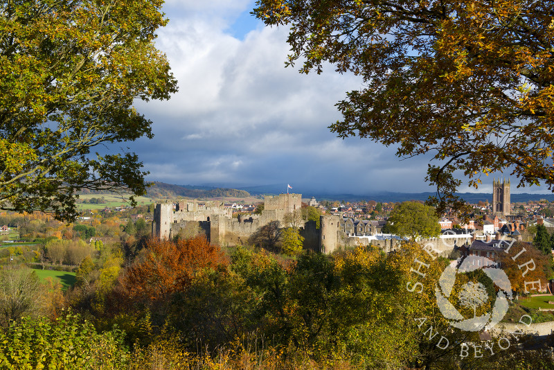 Autumn colours frame Ludlow Castle and St Laurence's Church as a shower of rain approaches from over Brown Clee Hill, Ludlow, Shropshire, England.