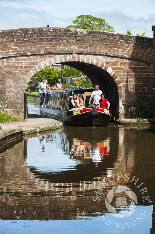 A canal boat and bridge are reflected in the waters of the Shropshire Union Canal at Market Drayton, Shropshire, England.