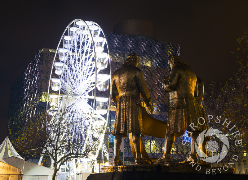 The bronze statue of Matthew Boulton, James Watt and William Murdoch in front of the Big Wheel and the Library of Birmingham during the Frankfurt Christmas Market, Birmingham, West Midlands, England.