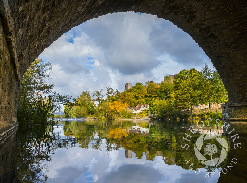 Ludlow reflected in the River Teme seen through one of the arches of Dinham Bridge, Shropshire.