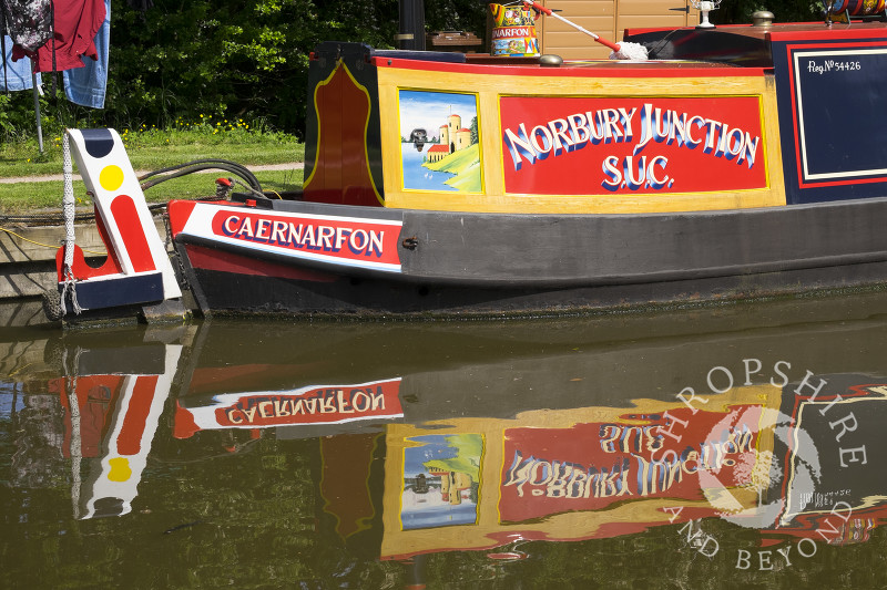 A canal boat reflected in the water of the Shropshire Union Canal at Norbury Junction, Staffordshire.