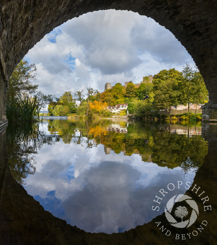 Ludlow reflected in the River Teme seen through one of the arches of Dinham Bridge, Shropshire.